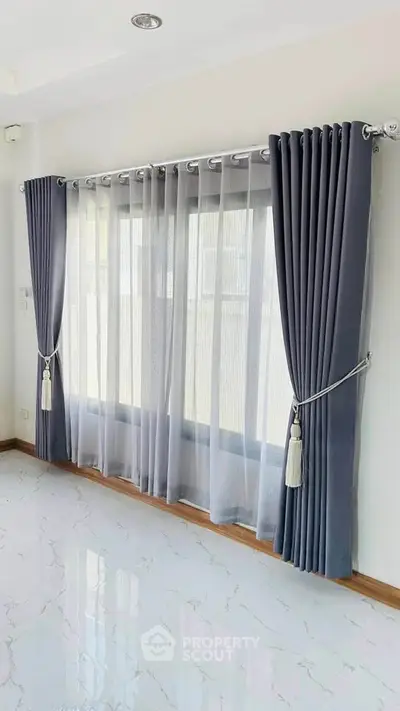 Elegant living room with large window and stylish curtains, featuring glossy marble flooring.