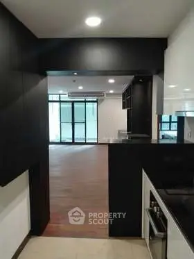 Modern open-layout kitchen leading to spacious living area with wooden flooring and large windows.