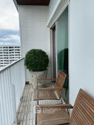 Charming balcony with wooden chairs and potted plant, offering a serene city view.