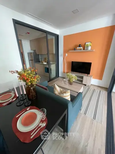 Modern living room with open kitchen, stylish decor, and vibrant orange accent wall.
