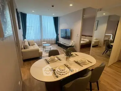 Modern open-plan living room with dining area and bedroom, featuring elegant decor and large windows.