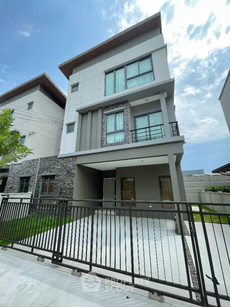 Modern three-story house with sleek design and gated driveway in a serene neighborhood.