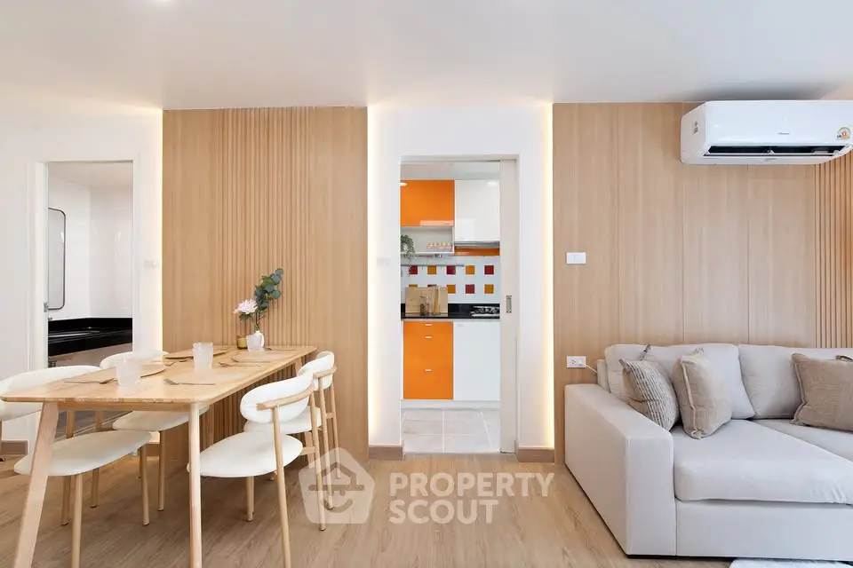 Modern living room with dining area and view into a stylish kitchen, featuring wood accents and bright decor.