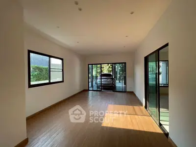 Spacious room with large windows and sliding glass doors leading to a garage, featuring natural light and wooden flooring.