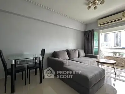 Modern living room with gray sectional sofa, glass dining table, and city view balcony.