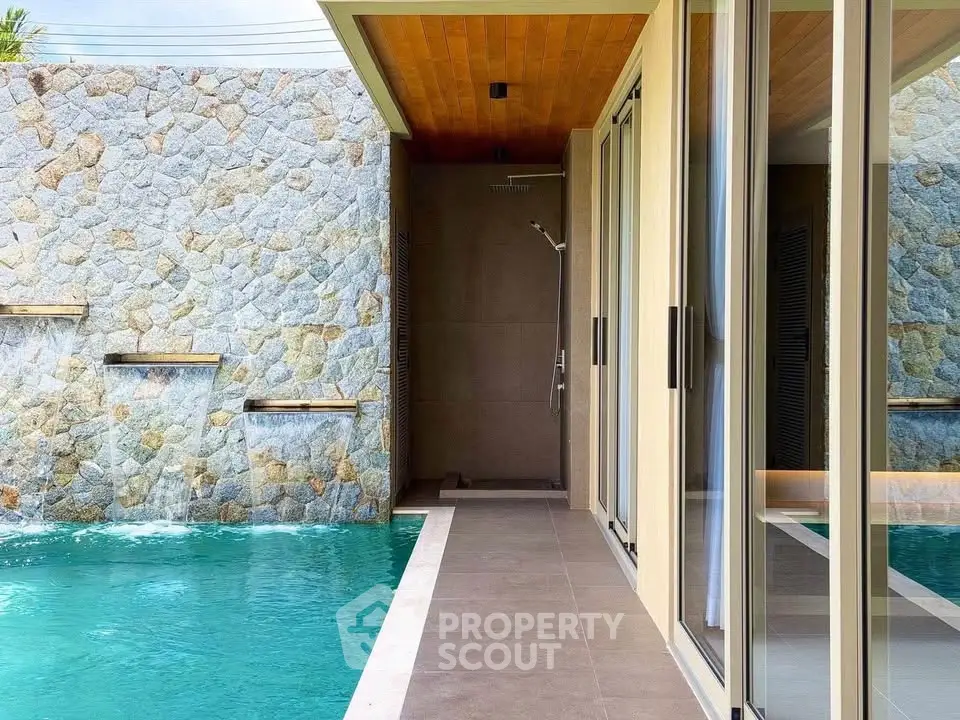 Luxurious modern villa with private pool and stone wall waterfall feature, perfect for relaxation and entertainment.