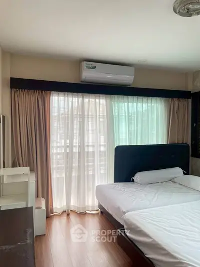 Spacious bedroom with large window and air conditioning, featuring modern furnishings and natural light.