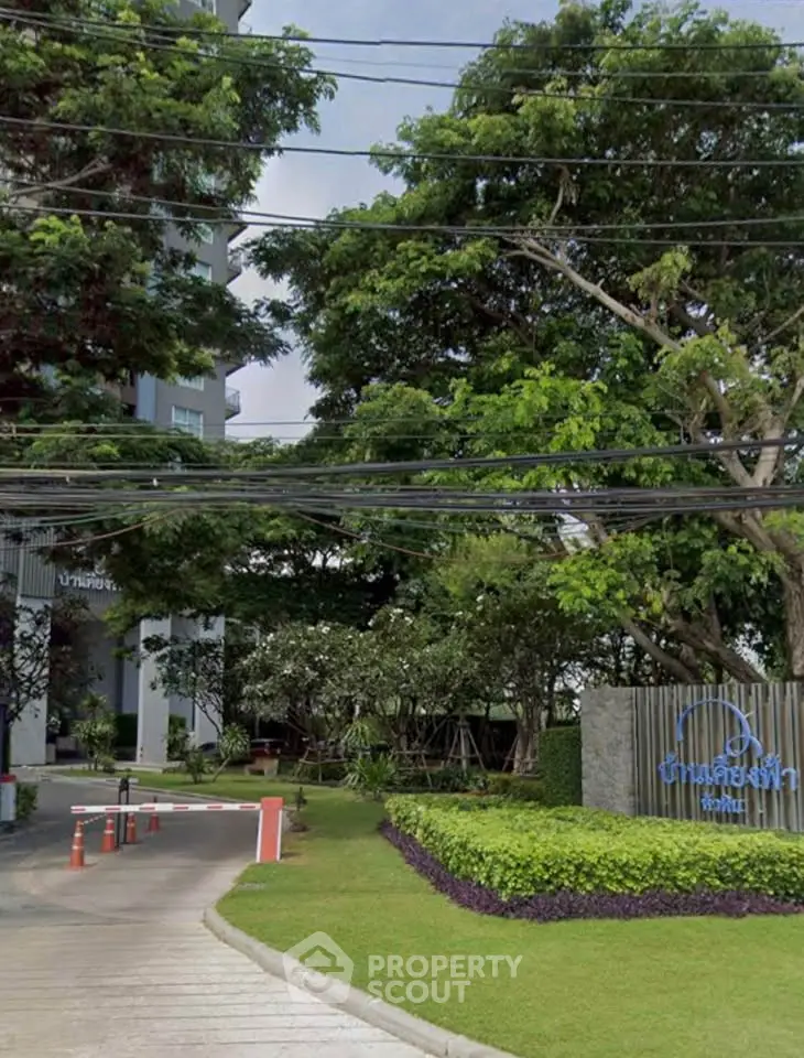 Lush green entrance of a modern residential building with trees and manicured lawns.