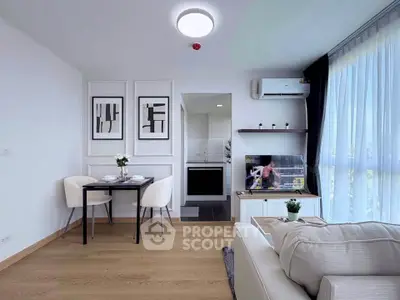 Modern living room with stylish decor and natural light, featuring a cozy dining area and sleek kitchen view.