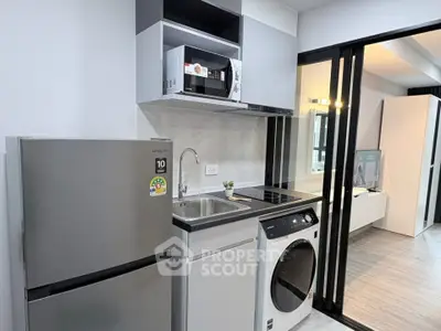Modern kitchen with sleek appliances including fridge, microwave, and washing machine in compact layout.
