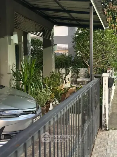 Charming residential entrance with lush greenery and covered parking space.