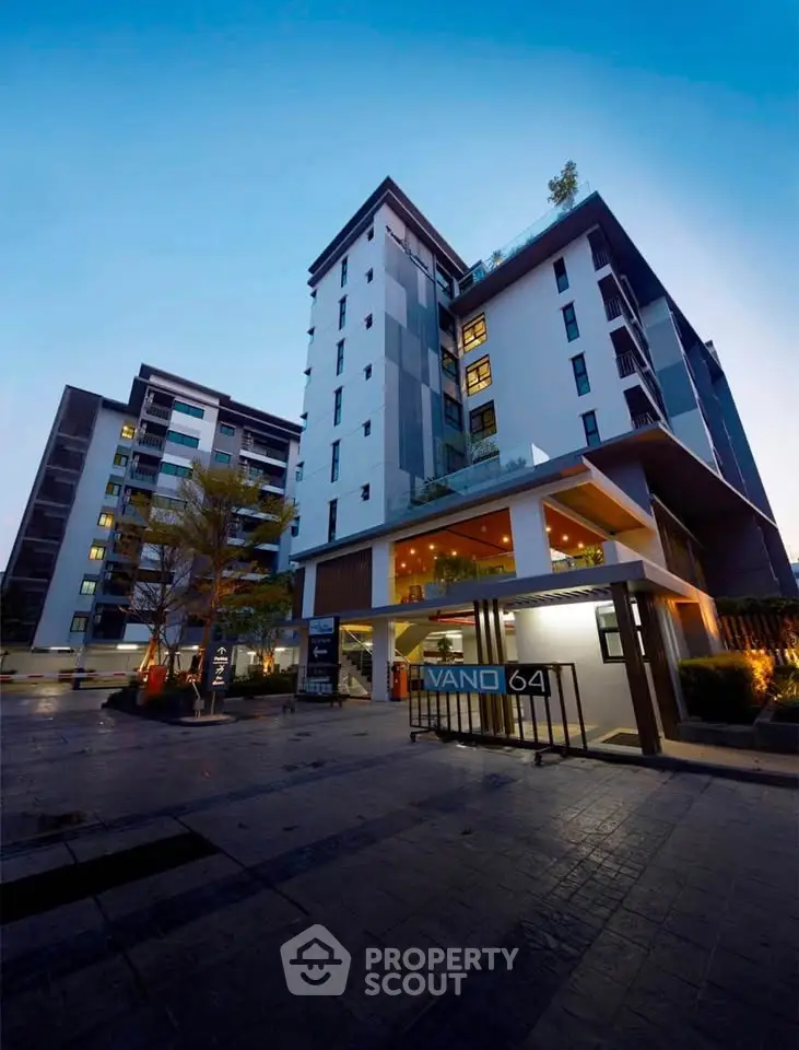 Modern high-rise building with sleek architecture and illuminated entrance at dusk.