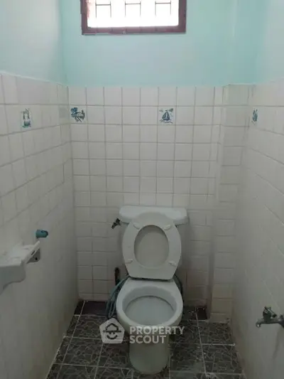 Compact bathroom with tiled walls and floor, featuring a standard toilet under a small window.