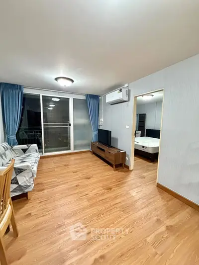 Spacious living room with wooden flooring and modern furniture, featuring a view into the bedroom.