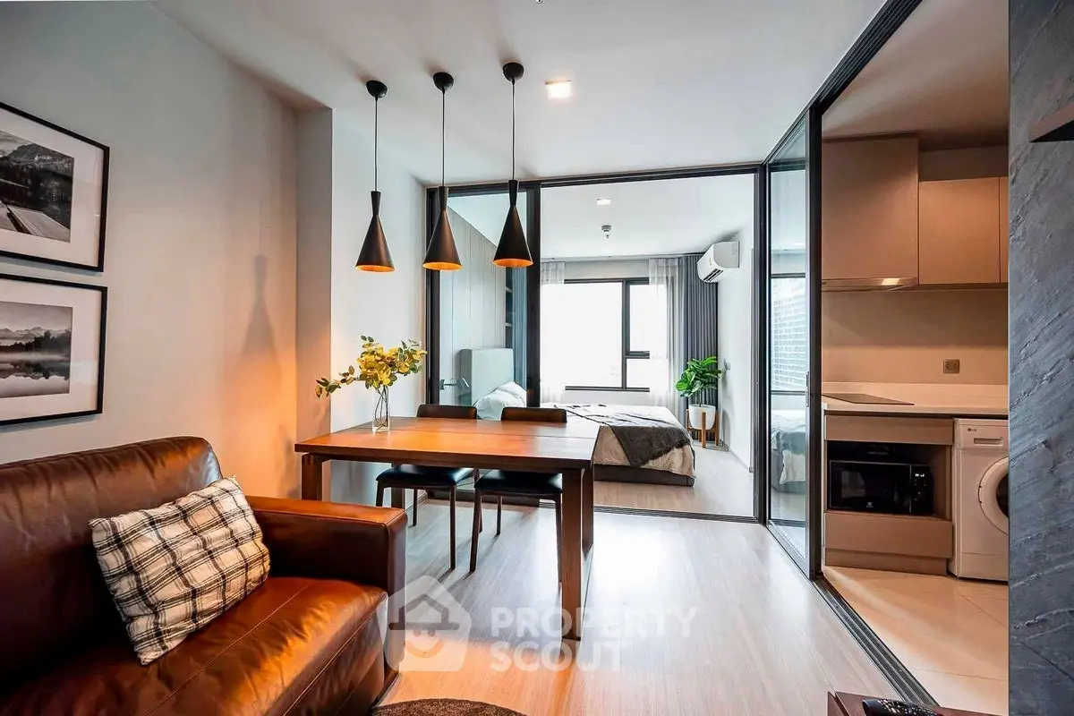 Modern open-plan living room with dining area and view into bedroom, featuring sleek design and natural light.