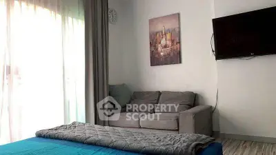Cozy bedroom with sofa and wall-mounted TV, featuring modern decor and natural light.