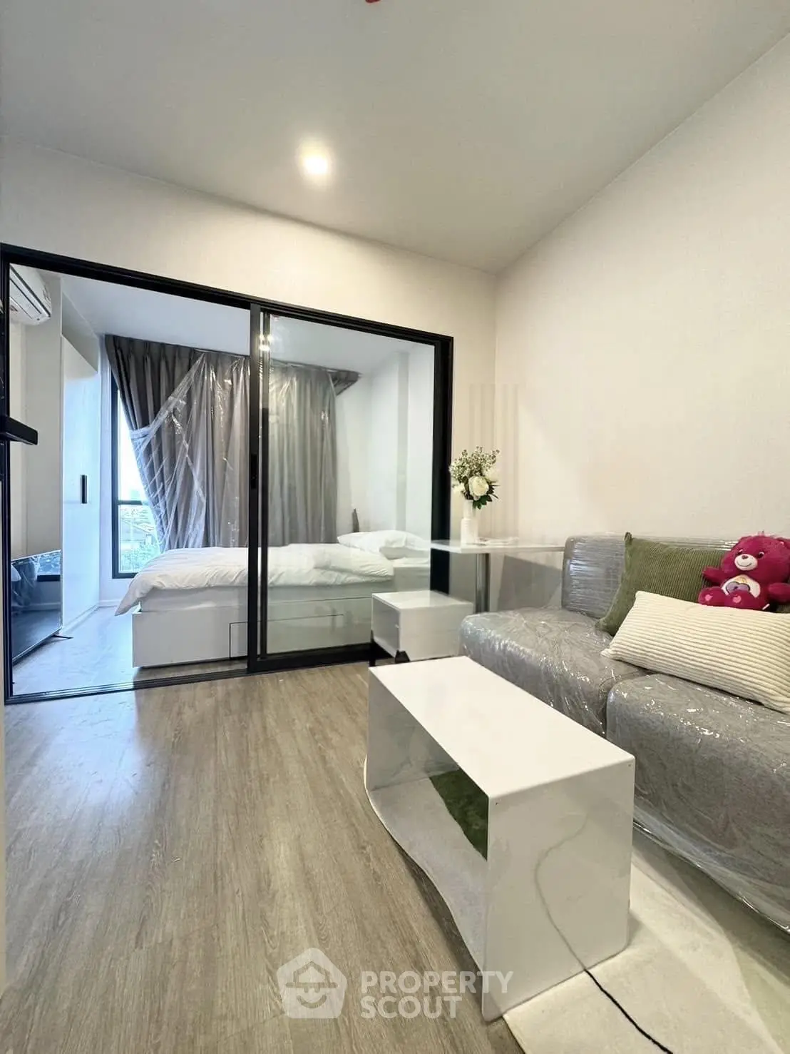 Modern living room with glass sliding doors leading to a cozy bedroom, featuring stylish decor and natural light.