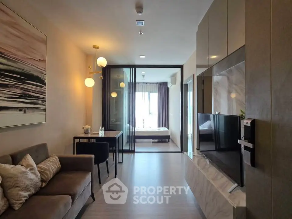 Modern living room with stylish decor and open view to bedroom, featuring sleek furniture and ambient lighting.
