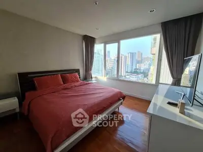 Spacious bedroom with city view and modern furnishings in high-rise apartment.
