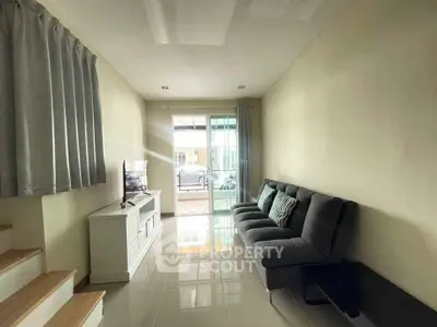 Modern living room with sleek sofa and TV, bright natural light through large windows.