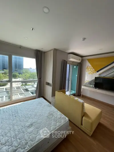 Modern bedroom with large windows and city view, featuring a cozy seating area and stylish decor.