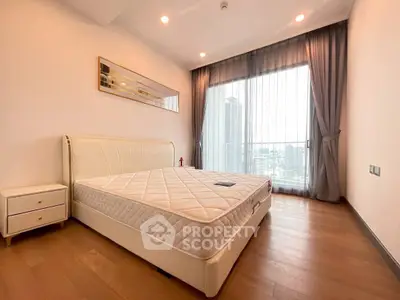Spacious bedroom with modern decor and city view, featuring a large window and elegant furnishings.
