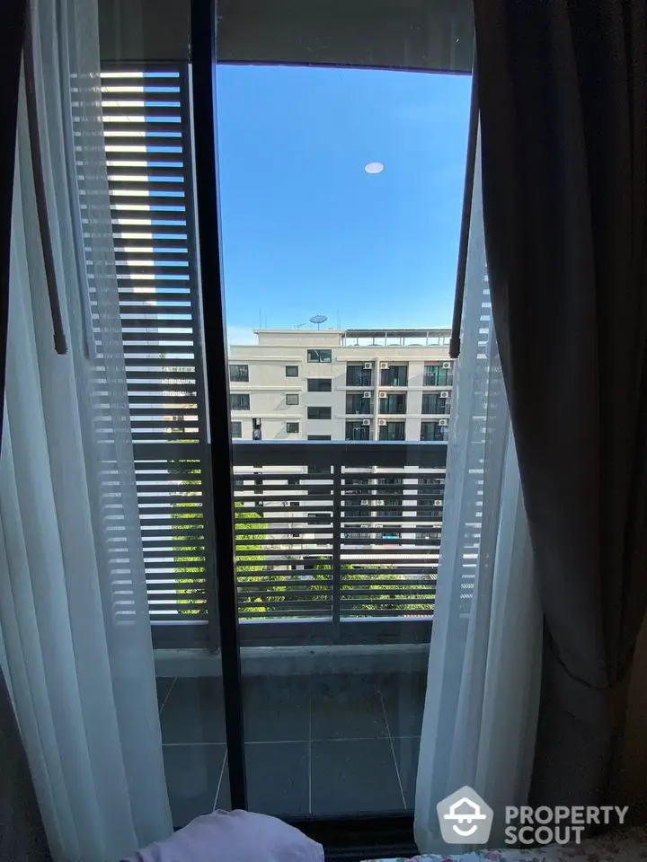 Modern apartment balcony with city view through glass doors and elegant curtains.