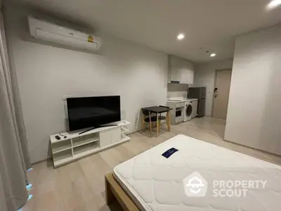 Modern studio apartment with open layout, featuring a TV, washing machine, and compact kitchen area.