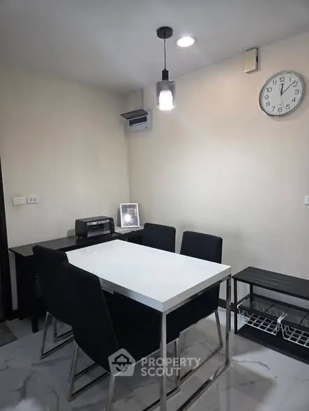 Modern dining area with sleek table and black chairs, featuring a wall clock and minimalist decor.