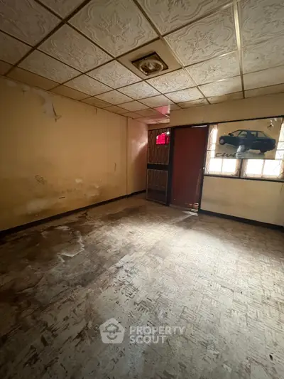 Spacious room with vintage ceiling tiles and natural light, ideal for renovation.