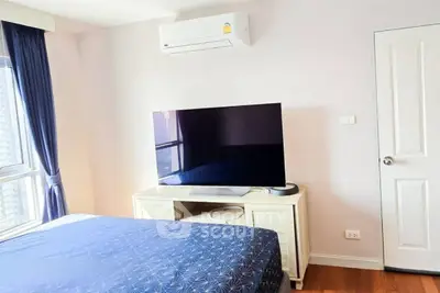 Modern bedroom with large TV and air conditioning, featuring stylish decor and natural light.
