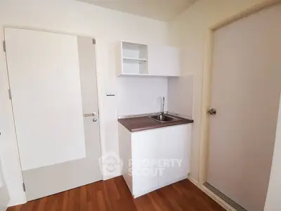 Compact kitchen with sleek white cabinetry and wood flooring in modern apartment.