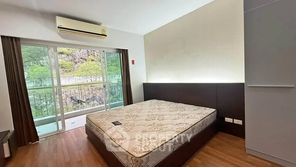 Spacious bedroom with large window and balcony access, featuring modern air conditioning and elegant wooden flooring.