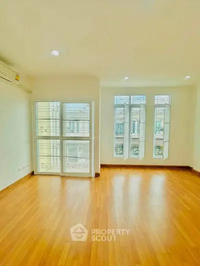 Bright and spacious room with large windows and wooden flooring, perfect for modern living.