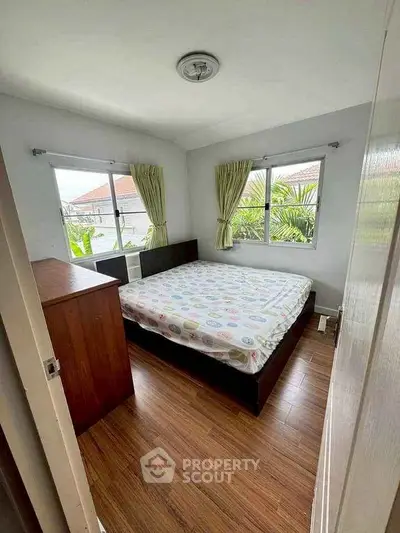 Cozy bedroom with wooden flooring and natural light from two windows.