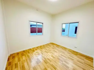 Spacious empty room with wooden flooring and large windows, perfect for customization.