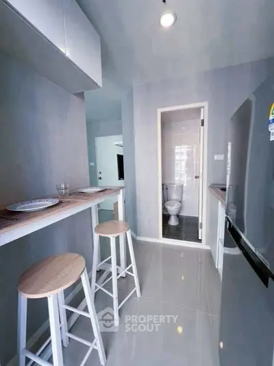 Modern compact kitchen with breakfast bar and stools, leading to a sleek bathroom.