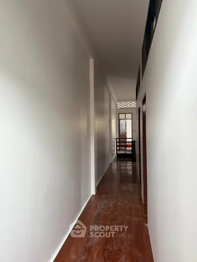 Spacious hallway with wooden flooring and white walls leading to a bright area.