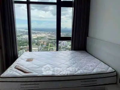 Spacious bedroom with large window offering stunning city view, featuring a comfortable mattress.