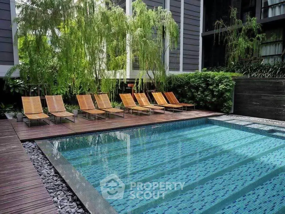 Luxurious outdoor pool area with stylish wooden deck and lush greenery in modern residential complex.