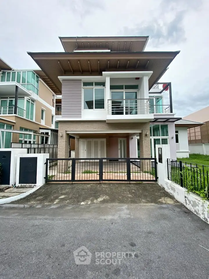 Modern two-story house with balcony and gated driveway in a suburban neighborhood.