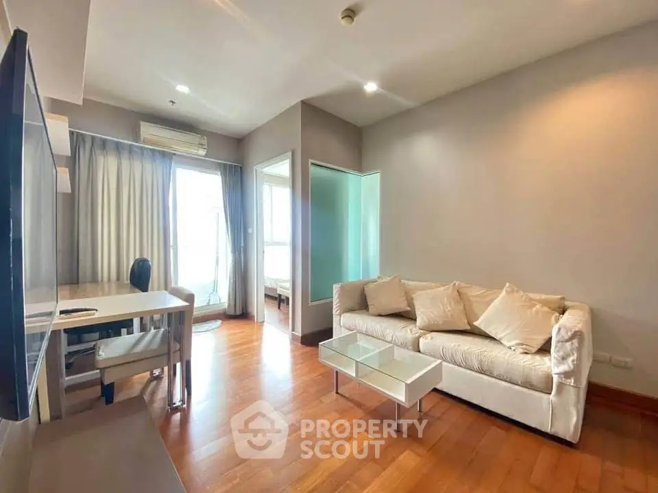 Modern living room with wooden flooring, cozy sofa, and natural light from large windows.