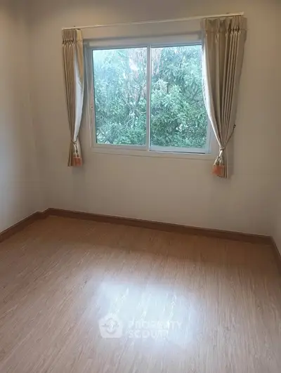 Bright empty room with large window and wooden flooring, ideal for customization.
