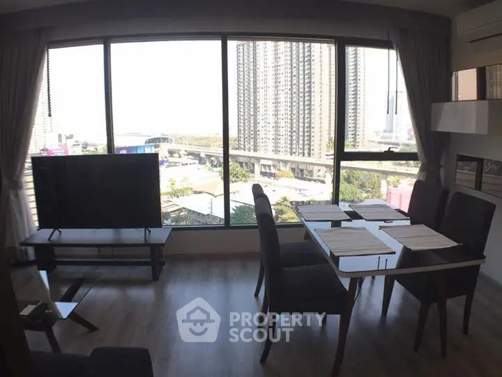 Modern living room with large windows offering stunning city views, featuring a sleek dining area and stylish decor.