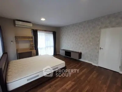 Spacious bedroom with modern decor and hardwood flooring, featuring a large window for natural light.