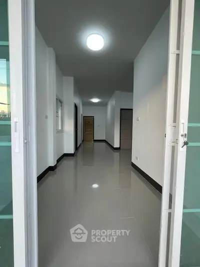 Spacious hallway with glossy tiled floors and modern lighting in a contemporary home.