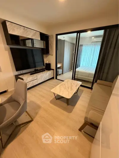 Modern living room with sleek furniture and glass partition leading to a cozy bedroom.