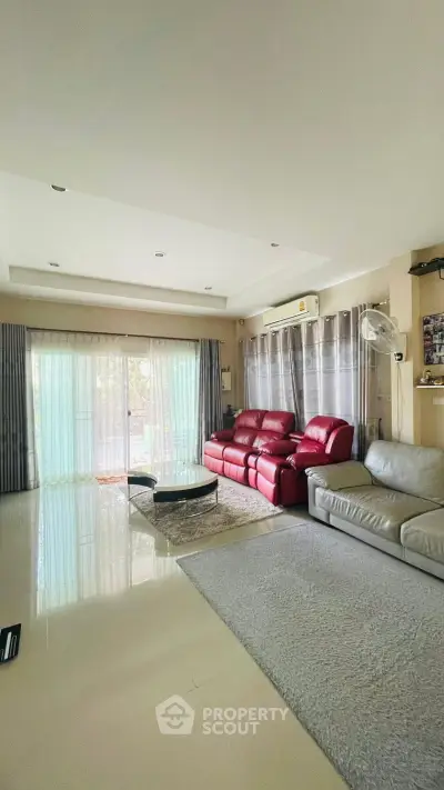 Spacious living room with modern red and gray sofas, large windows, and elegant decor.