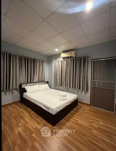 Spacious bedroom with modern decor and wooden flooring, featuring a comfortable bed and air conditioning.