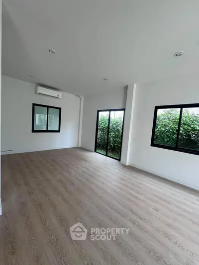 Spacious unfurnished living room with large windows and wooden flooring, perfect for customization.